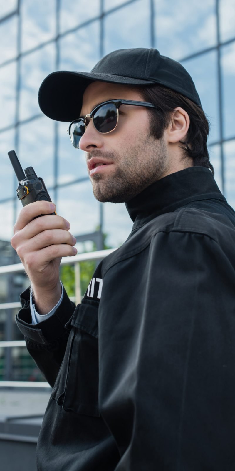 serious guard in sunglasses and black uniform talking on radio set outdoors